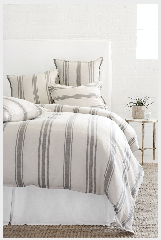 A bed with a big fabric head board, with flax and midnight striped duvet and pillows