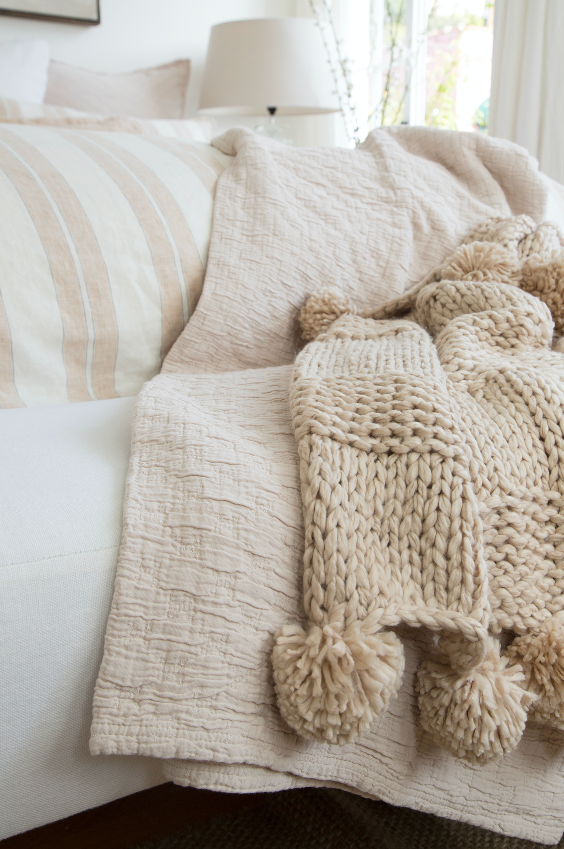 A blush blanket and a taupe knit blanket with pom poms