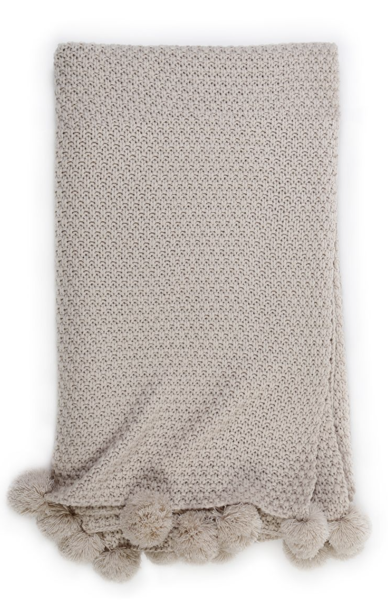 A knit taupe throw with pom poms on the edge.