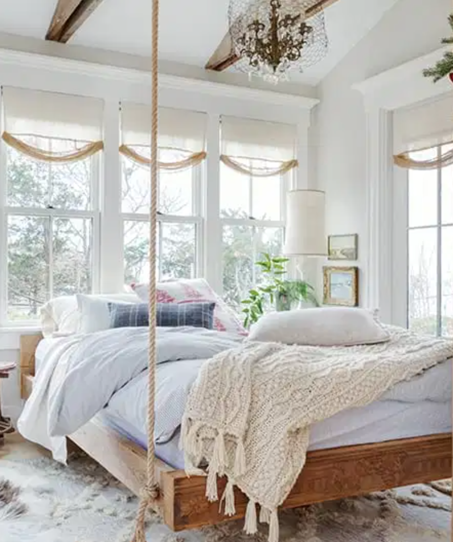 a wooden platform bed hanging by ropes in a cape cod bedroom
