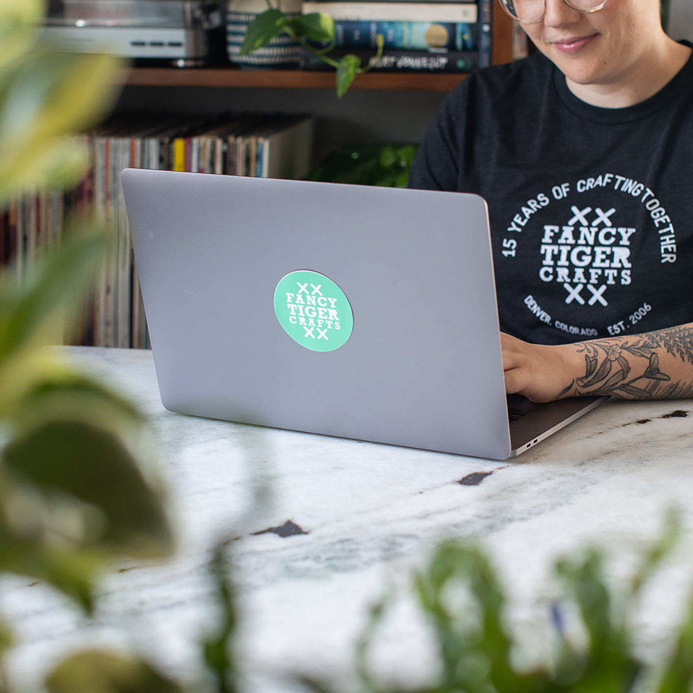 This is an image of a person sitting at a laptop with a Fancy Tiger Crafts sticker on the outside of the top of the laptop.