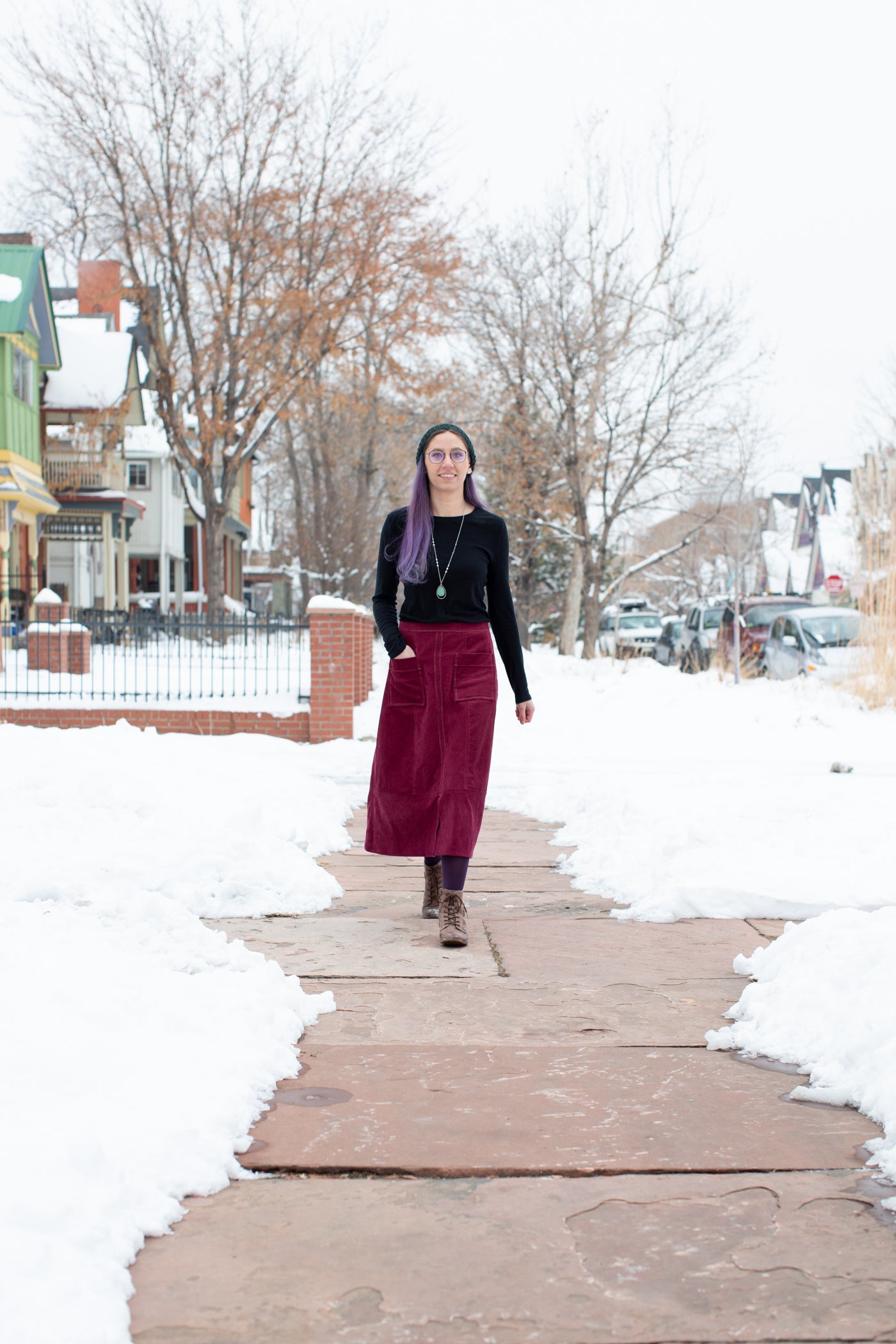 Aly is walking down a city sidewalk, with snow on both sides of the sidewalk.  Aly is wearing a Robert Kaufman Corduroy skirt in merlot with a black long sleeve top.   