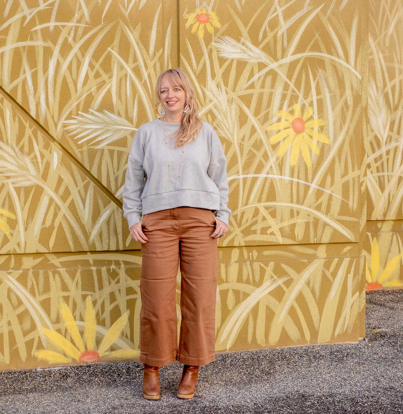 Amber wearing the Hosta sweatshirt—a slightly cropped, long sleeve, crew neck top—brown wide leg pants, and clog boots.