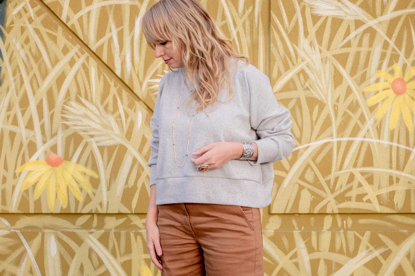 Close up of Amber wearing a grey Hosta sweatshirt, with sleeves pushed up slightly and arm bent.