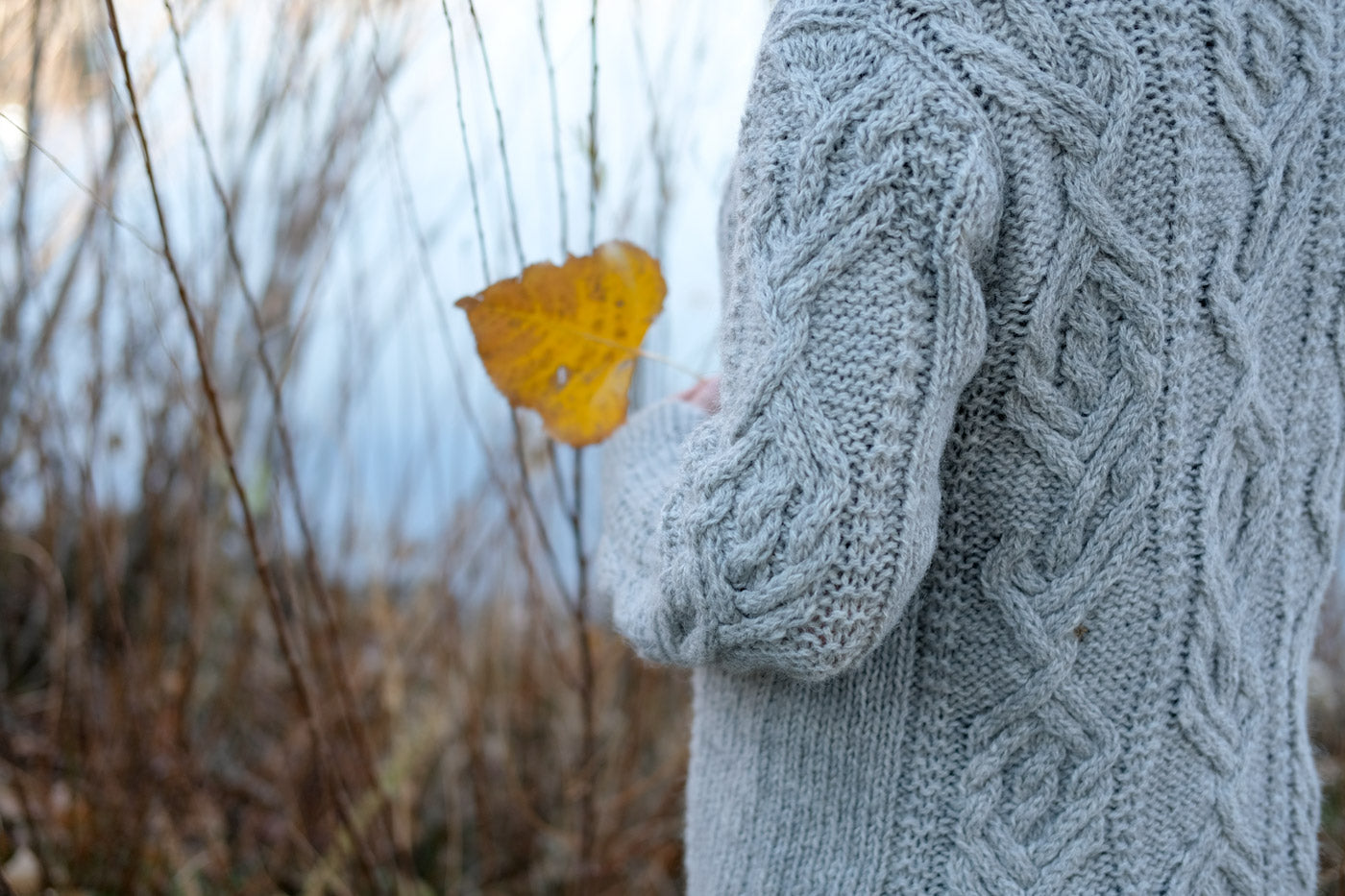 The elbow and shoulder of Amber's Junegrass Sweater while she holds a leaf