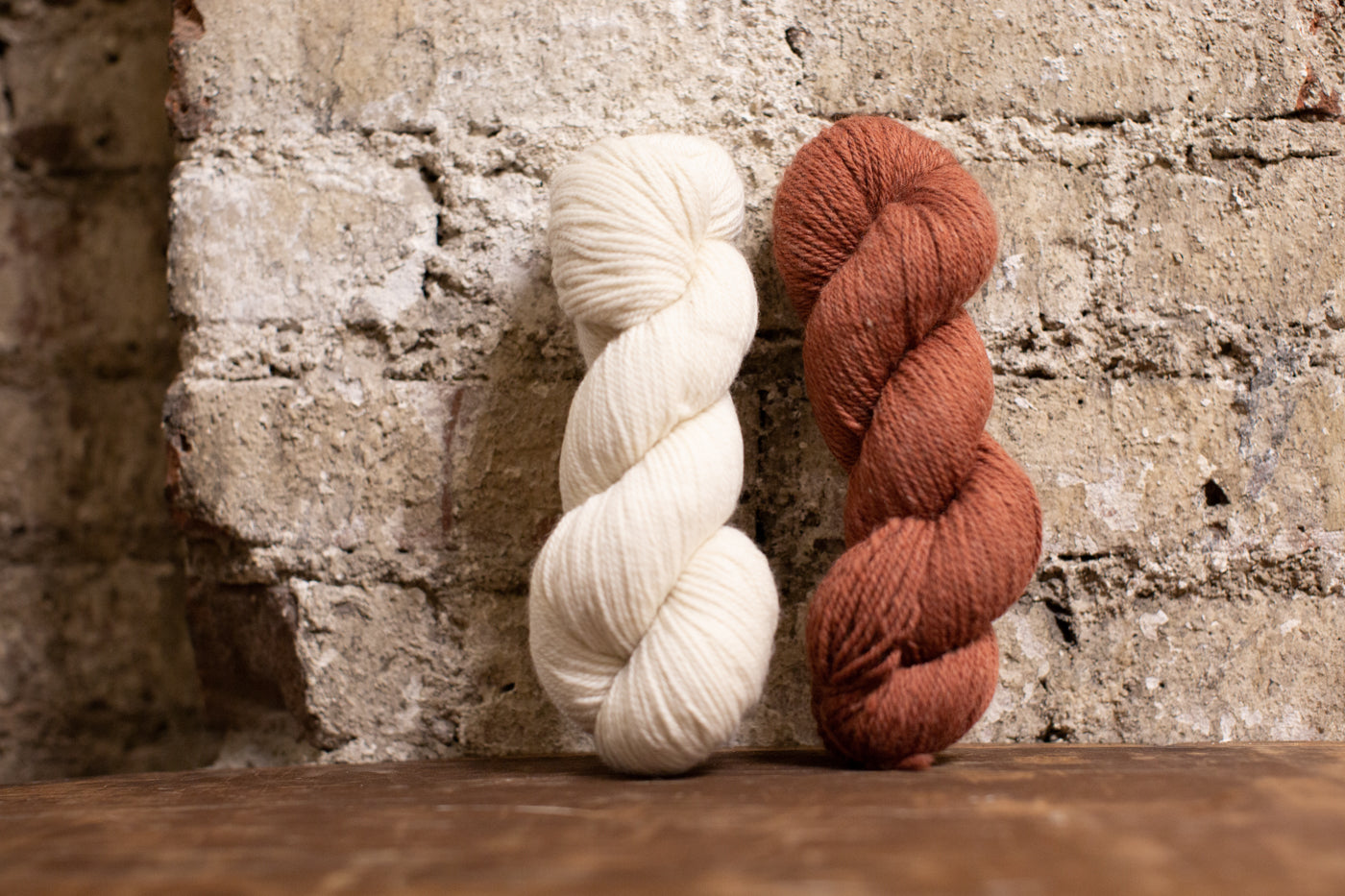 White yarn and muted red yarn leaning against a white wash brick wall.