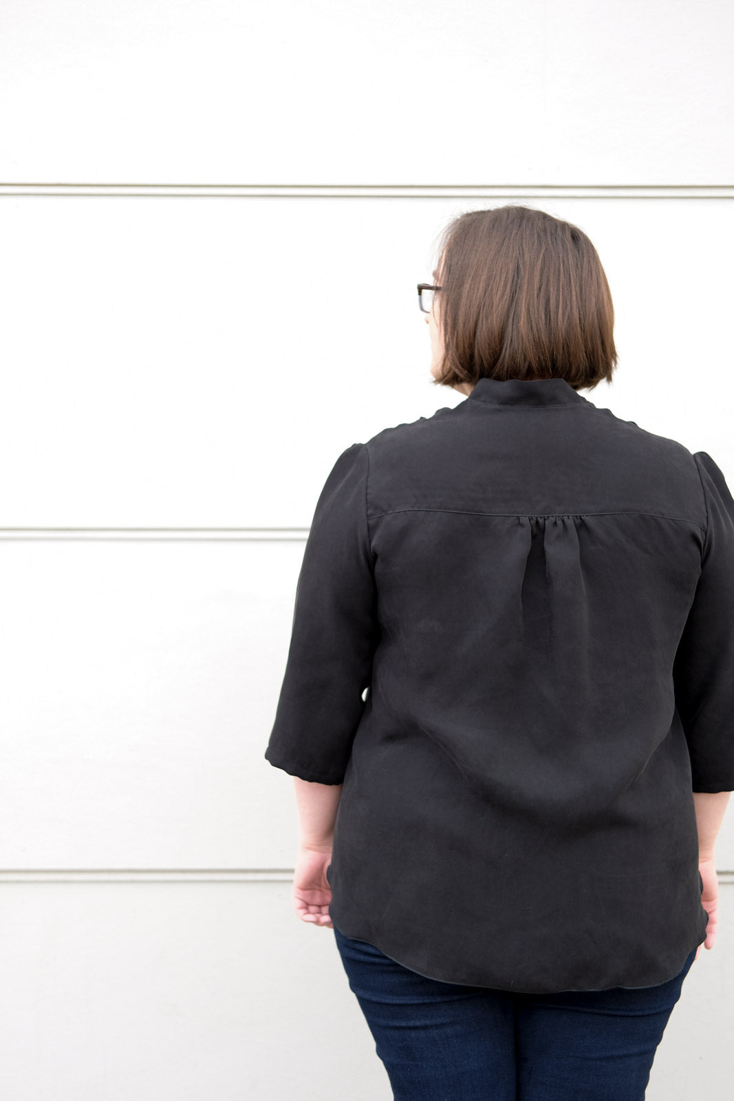 Close up of the back of a woman wearing a drapey black blouse, showing the gathered yoke. 