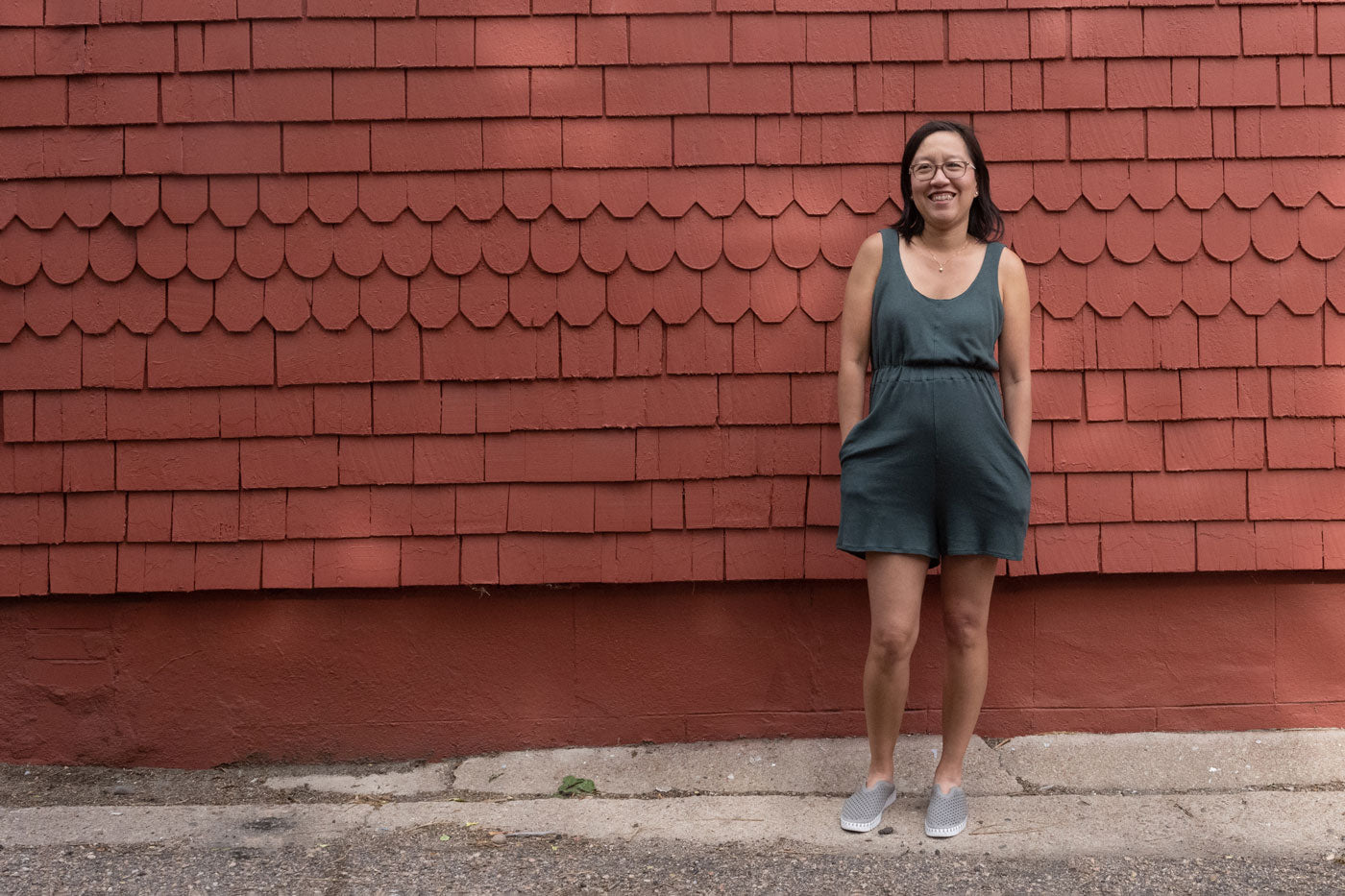 Jenn stands in front of a red wall wearing her Nova jumpsuit with her hands in her front pockets