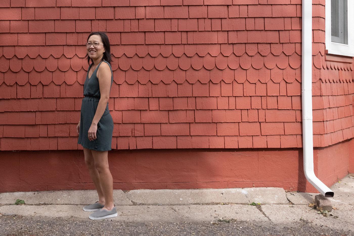 Jenn stands in front of a red wall, facing sideways, wearing her Nova Jumpsuit.