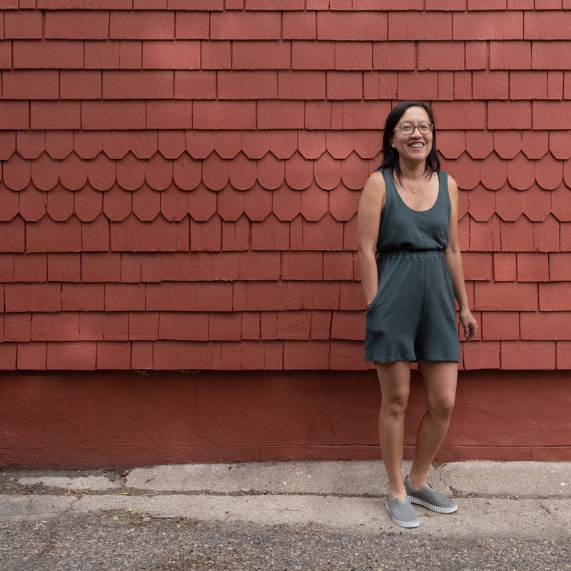 Jenn stands in front a red wall wearing her Nova Jumpsuit with her hands in the pockets