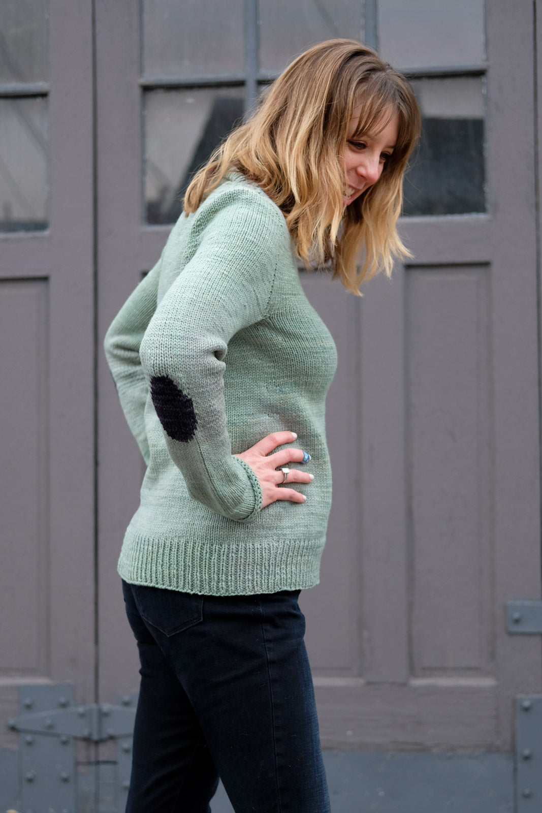 View of Lizz in her Molly Sweater- Hands on hips showing off her knit-in elbow patch
