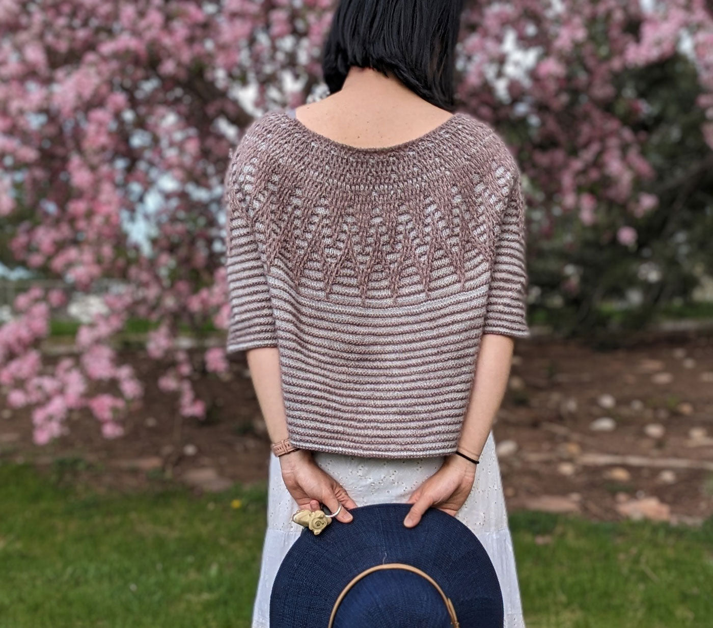 This a close up shot of the back of Connie's Aubade sweater. She holds a navy wide prim hat in her hands.