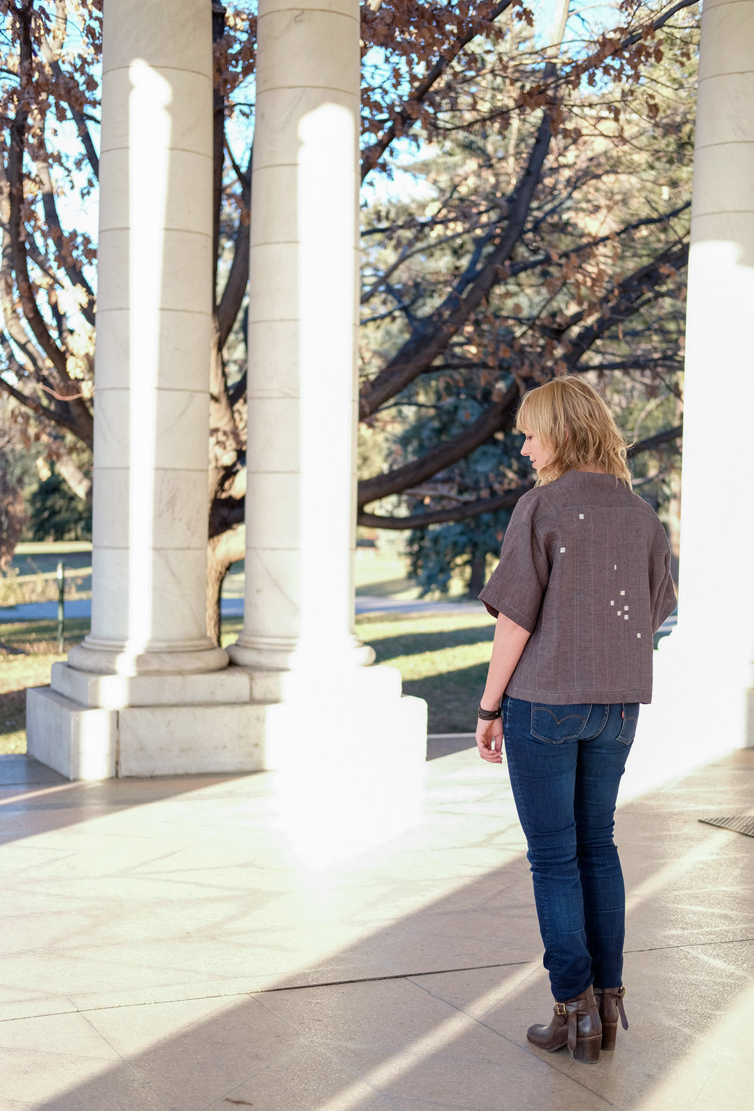 Amber Corcoran Platzer standing between two columns showing off the back of her grey linen Hoshi Jacket