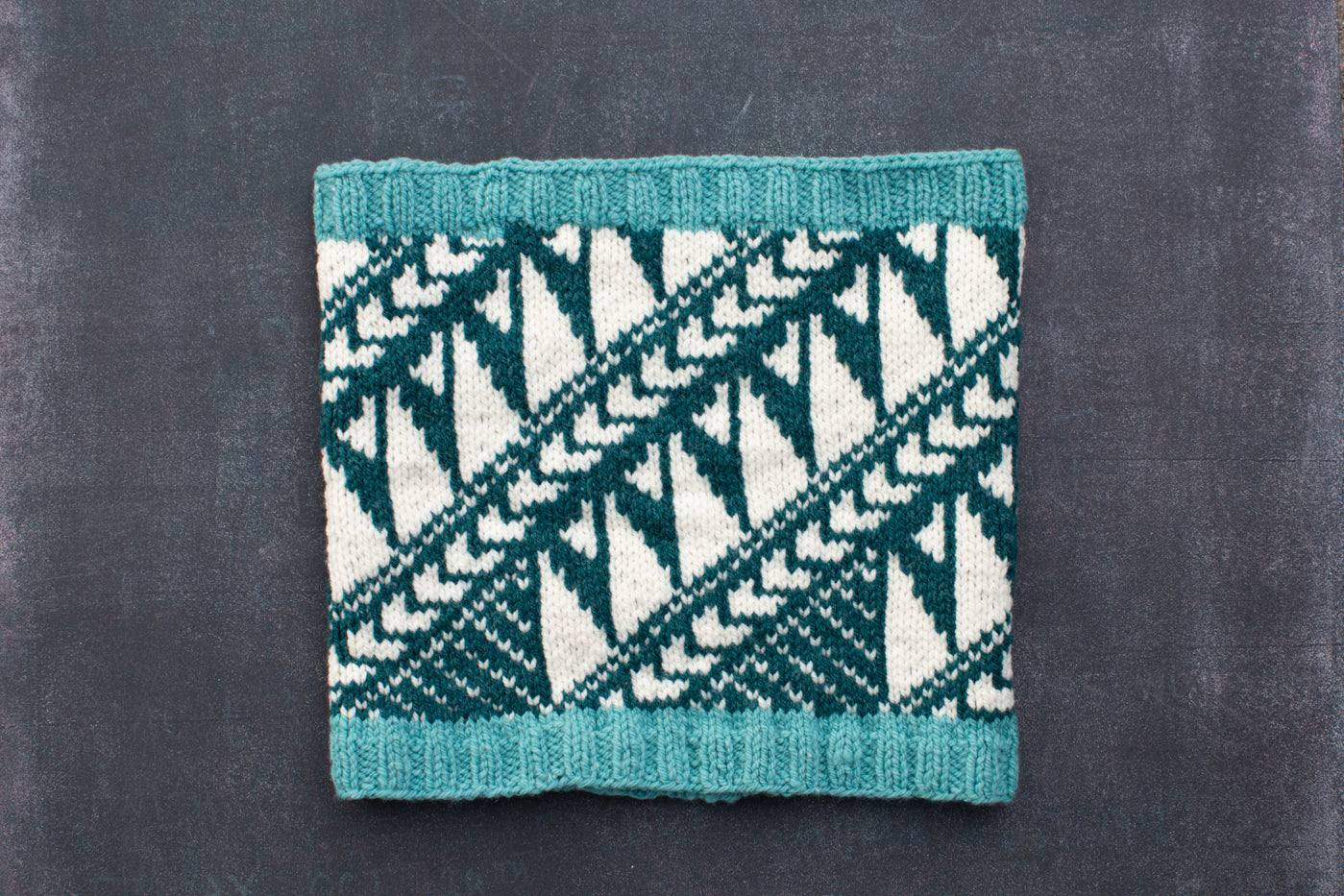 Cowel in knitted in white, turquoise and teal on a black background.