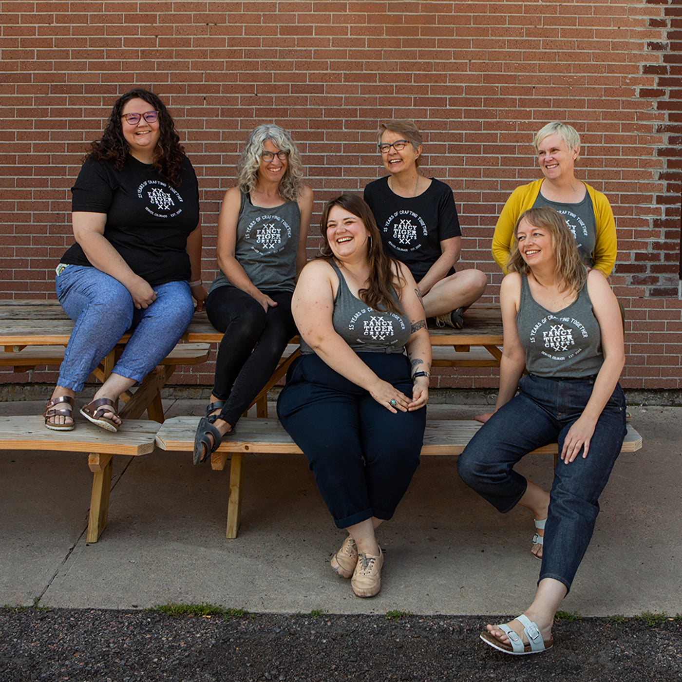 This is an image of women wearing Fancy Tiger Crafts shirts sitting on benches in front of a brick wall. 