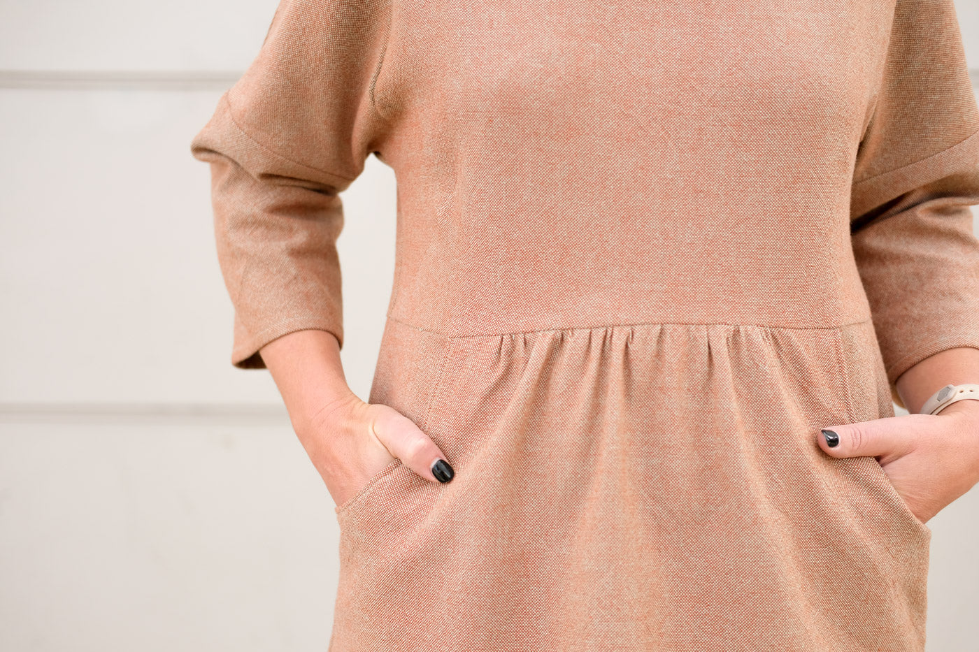 Detail of the waist and pockets of the Fen dress. It shows a close up of the subtly textured, plain weave fabric, and Jaime's hands in the waist pockets.