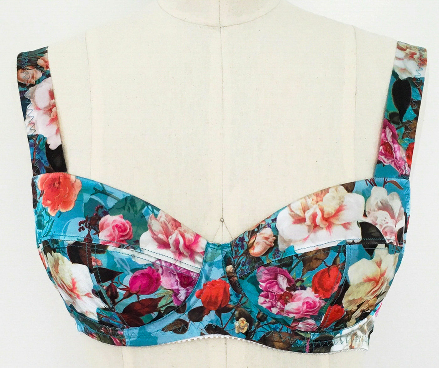 Close up of a dress form with a vibrant aqua and peach floral underwire bra.