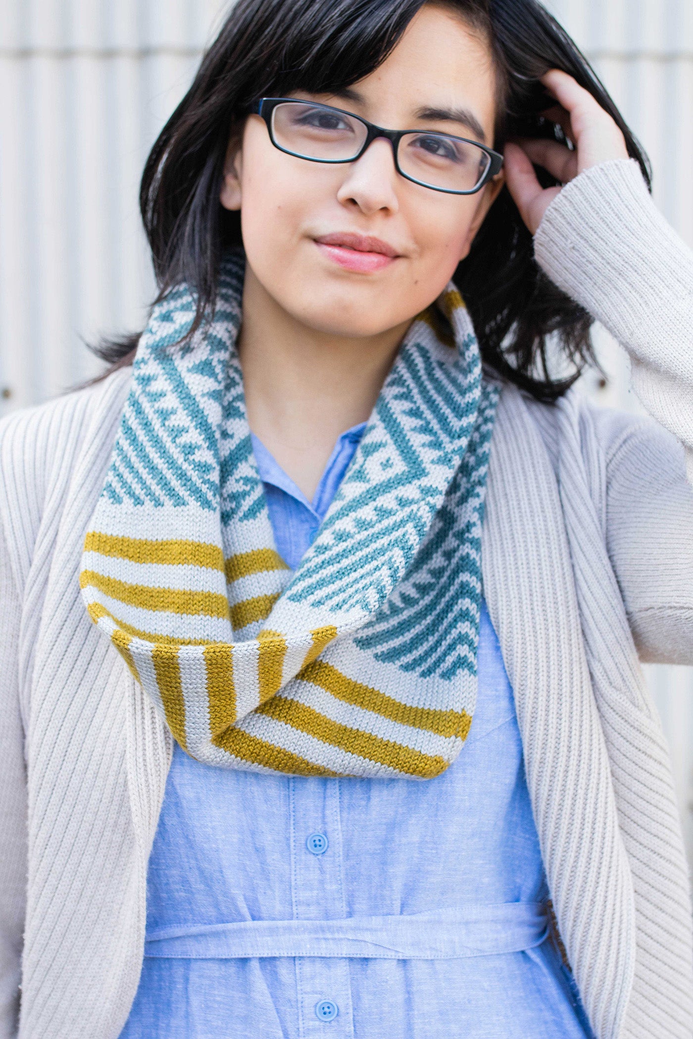 Portrait photograph of women wearing glasses and hand in her hair.  Wearing a light demin dress, light colored knitted shawl.