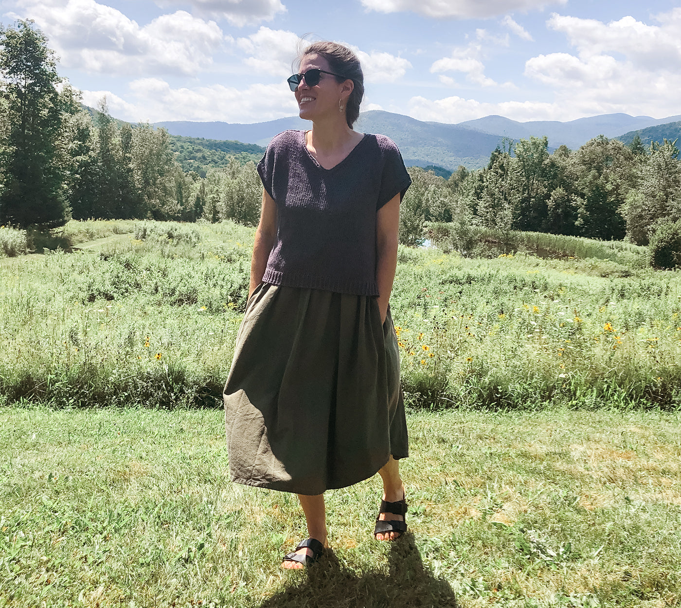 This is an image of a woman standing in a field with clouds behind her. 