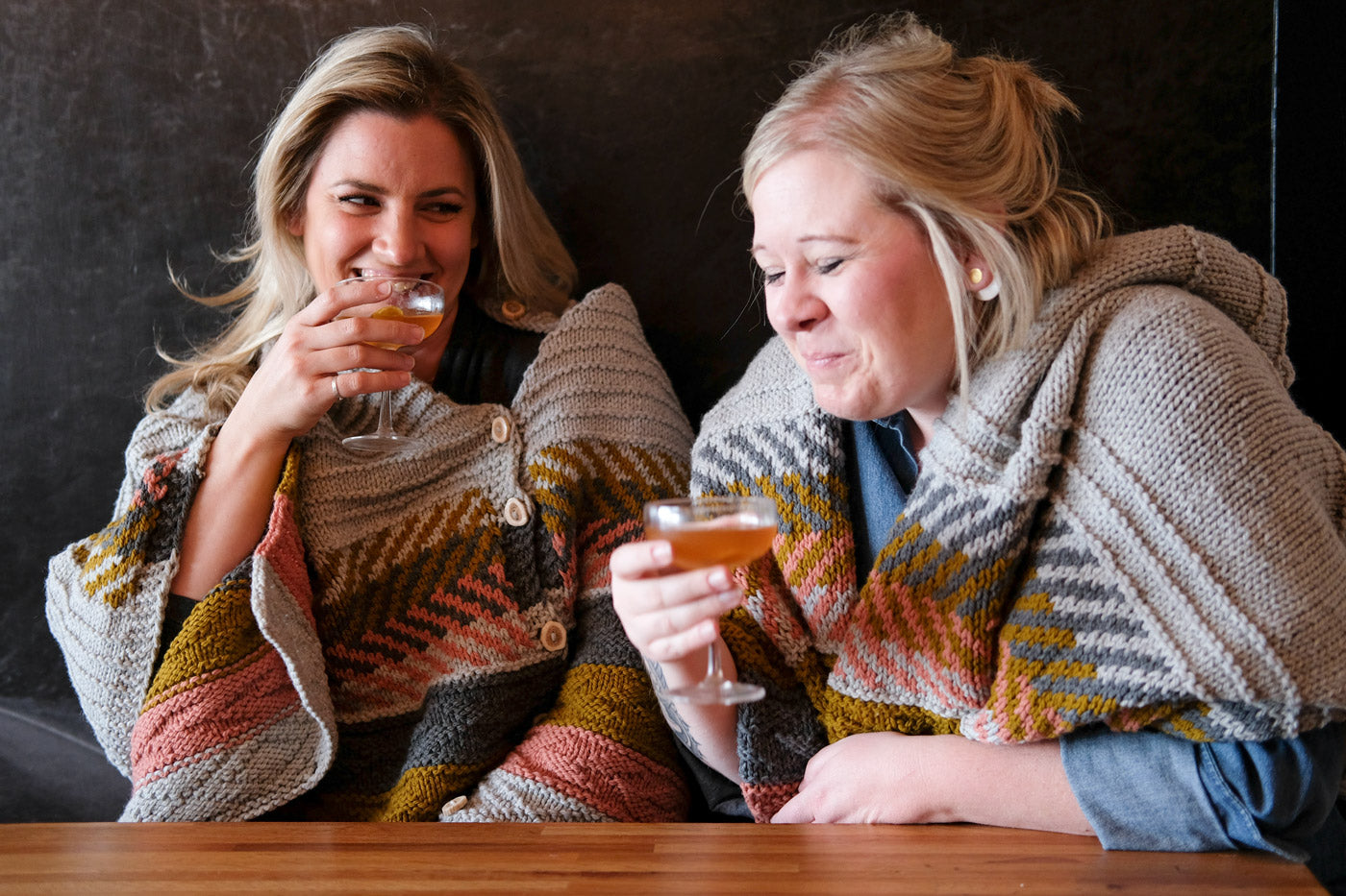 Kelly and Heather sipping cocktails in their Om shawls