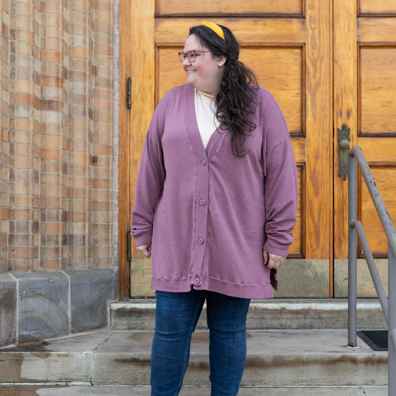 This is an image of Kim wearing her Marlo Sweater in rayon cotton modal sweater knit in Rose brown. She is standing on steps in front of a light brown door. She is also wearing a yellow headband, a white shirt underneath her cardigan, and blue jeans. 