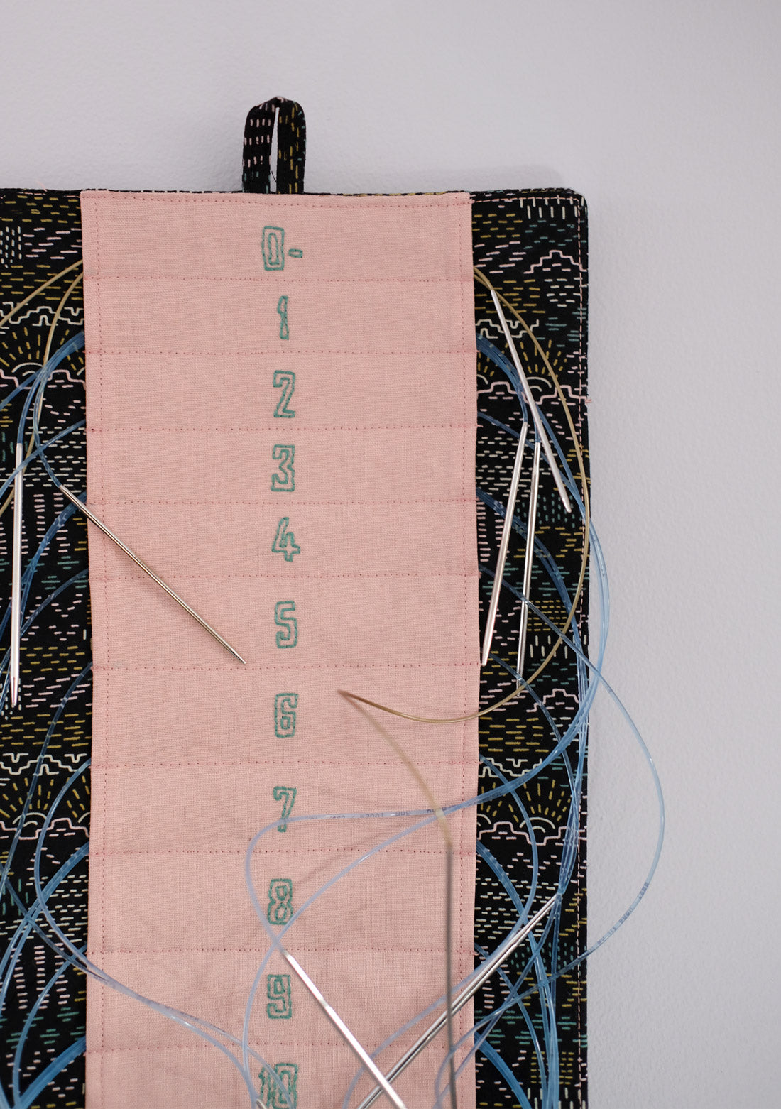 Close up photo of the pink and black knitting needle minder with hand embroidered needle numbers