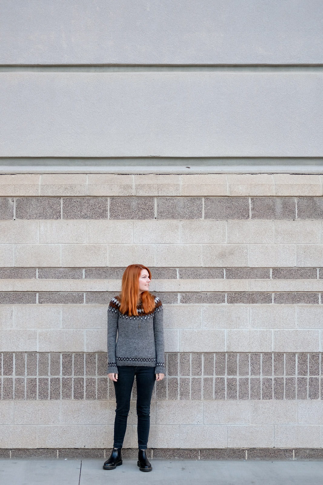 Lauren against a tall tan brick wall in her Treysta Colorwork Sweater