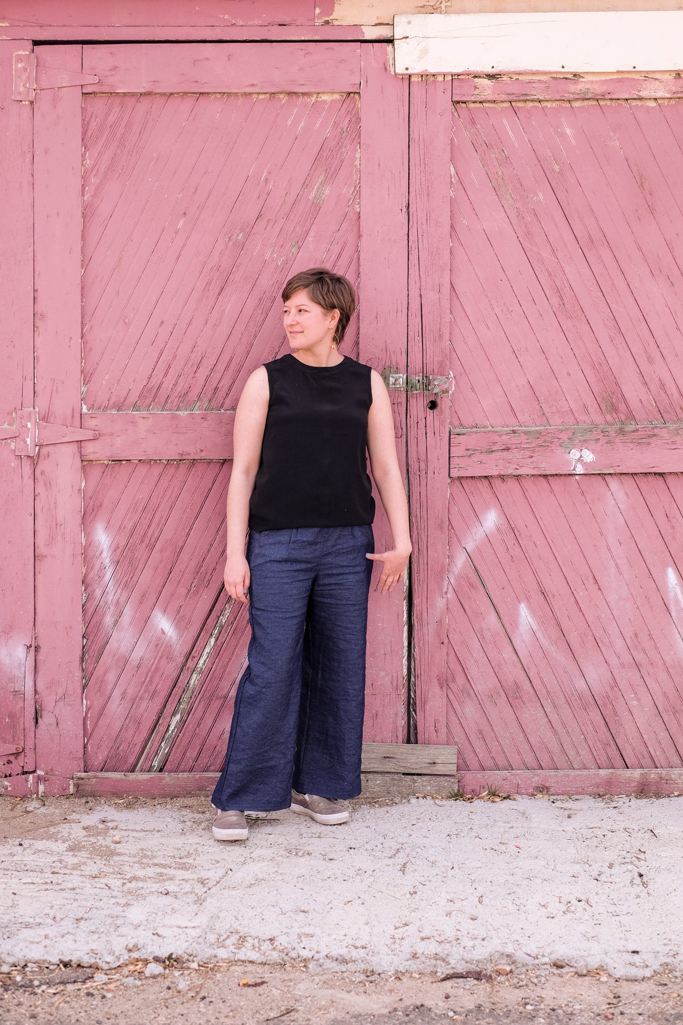 Lucy standing in front of a weathered red barn door wearing her indigo linen Emerson trousers