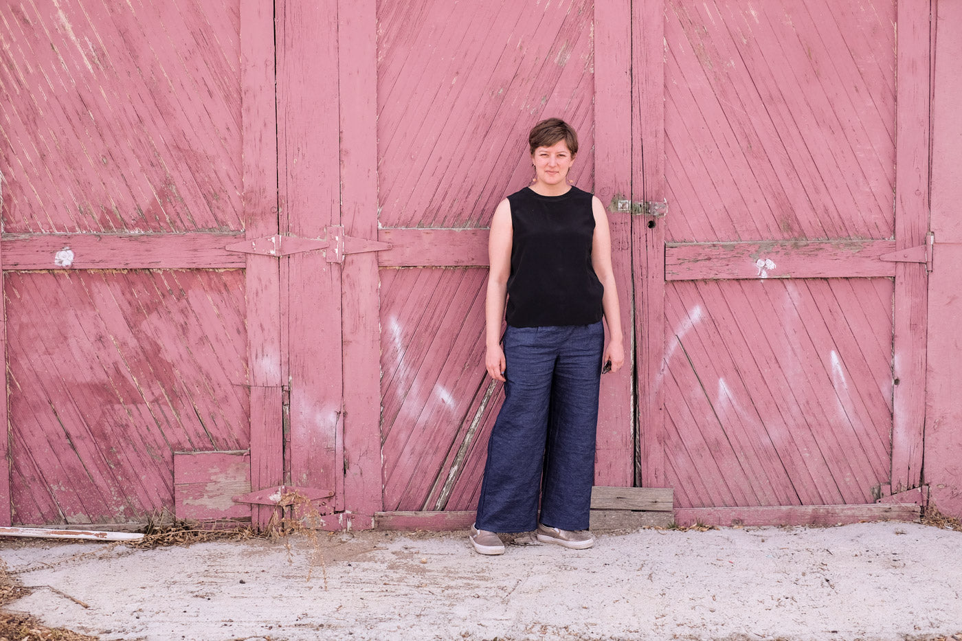 Lucy wearing her indigo linen trousers, she stands in front of a weathered barn door.