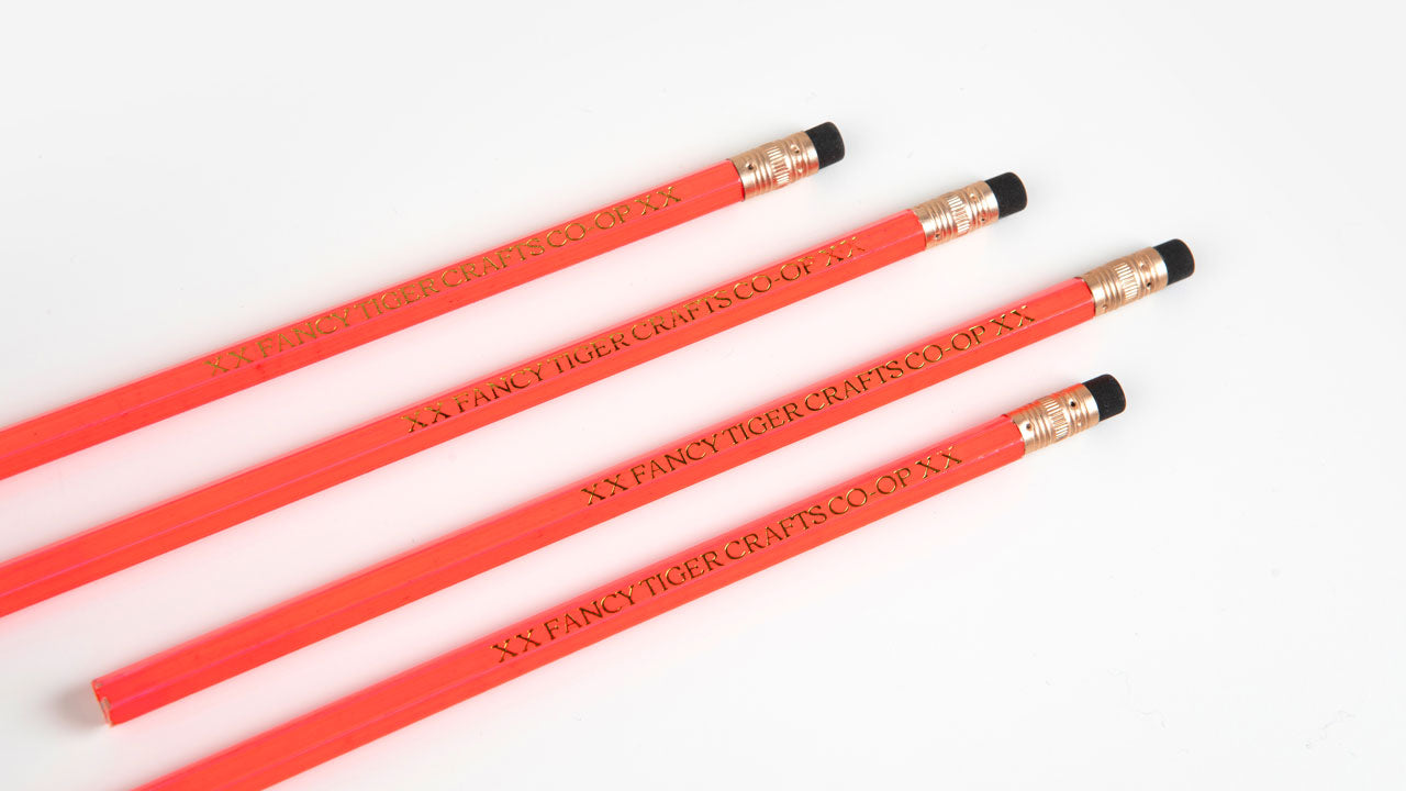 Four orange pencils with the text "XX Fancy Tiger Crafts Co-Op XX are placed diagonally next to each other on a white background