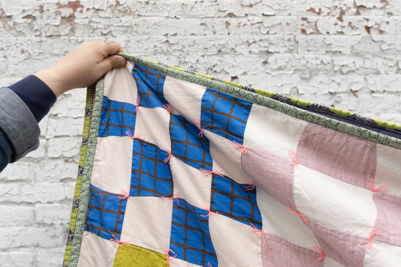 A close up shot of a hand holding up a corner of the quilt