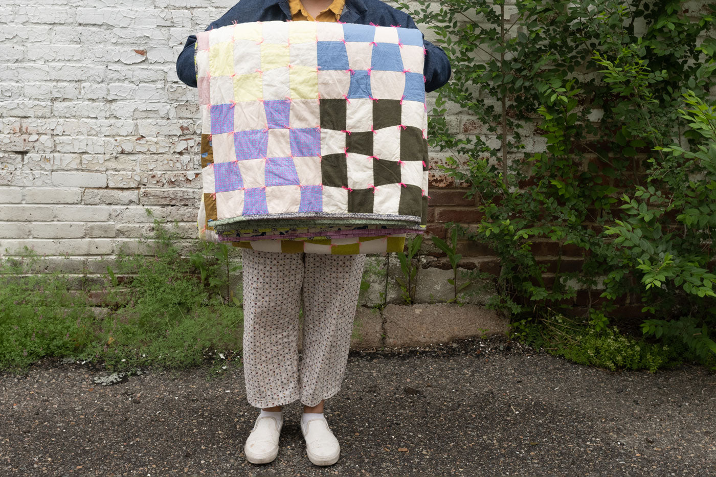 Shawna's Omega quilt is folded over a person's arm. They stand in front of a white brick wall. 
