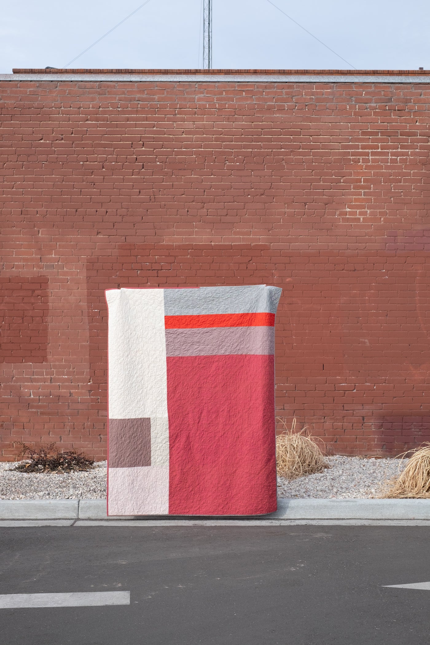 Scrap quilt showing the back of the quilt.  Large color blocks make up the back of the quilt.  Quilt is being held up in front of a red brick wall.