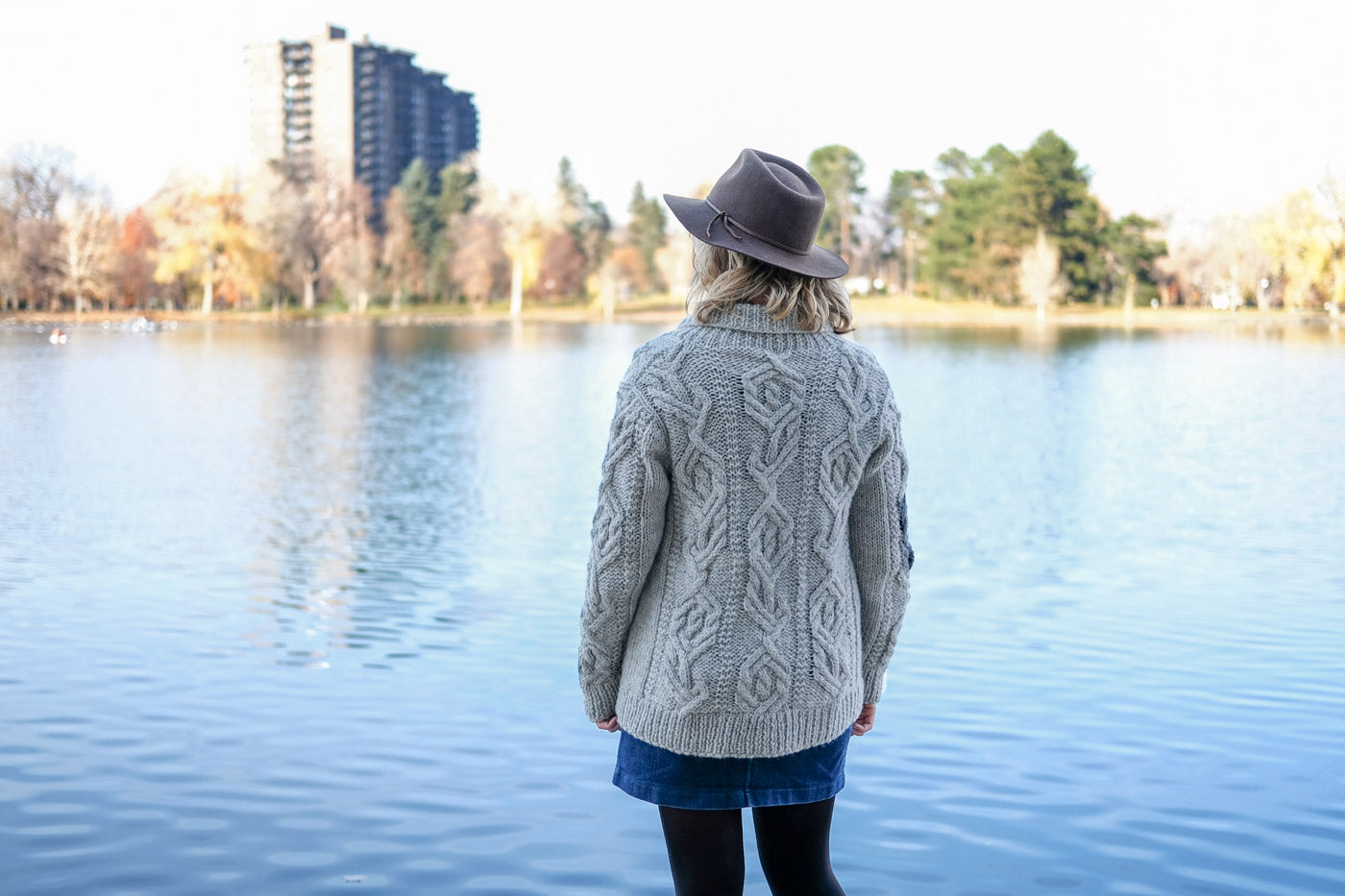 Amber looking out over a lake showing off the back side of her cabled cardigan