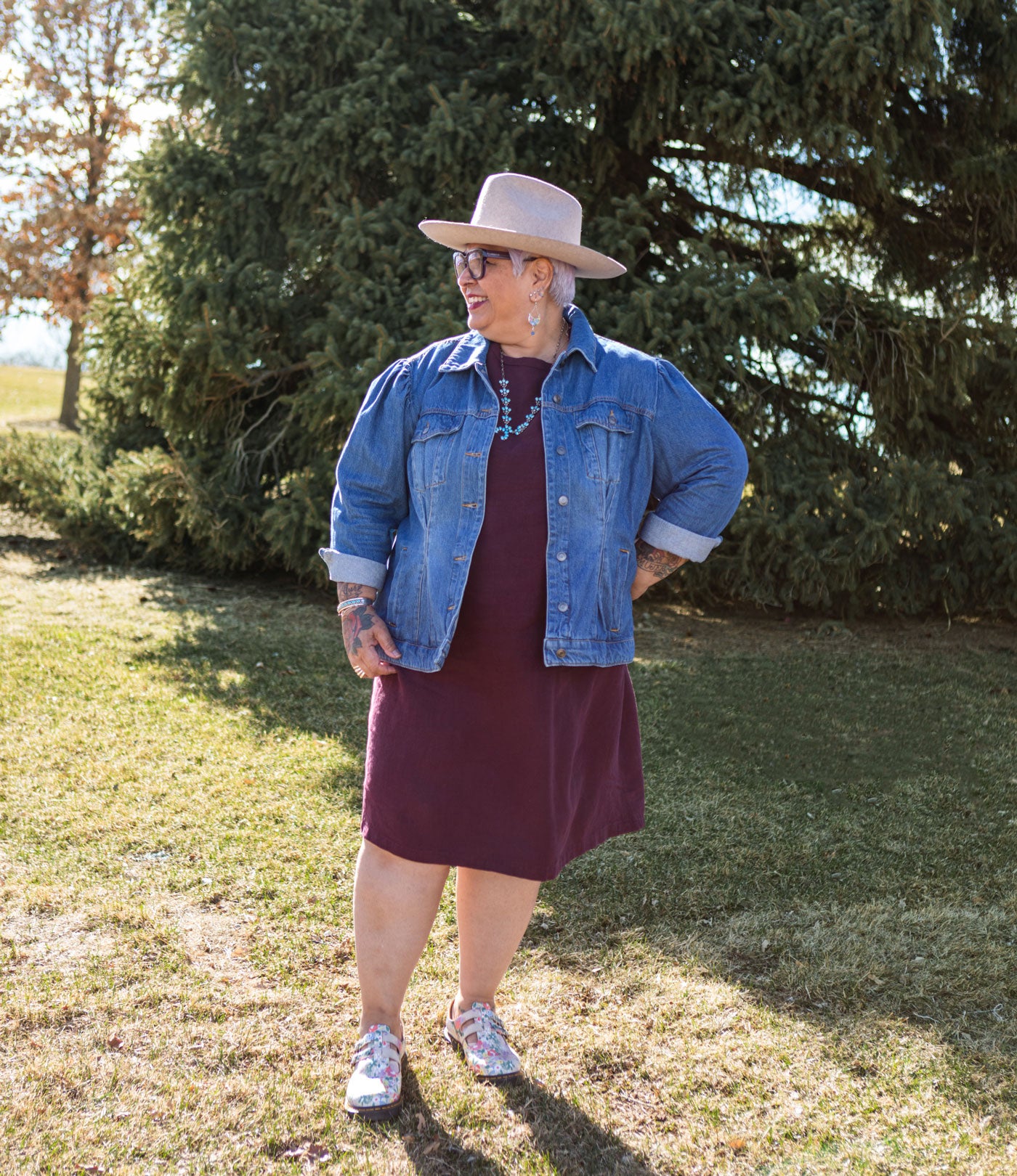 This is an image of Yolanda wearing her Camber Set dress in Nomad Linen.  Twill in Merlot. She is wearing a jean jacket over it and a light brown hat.  