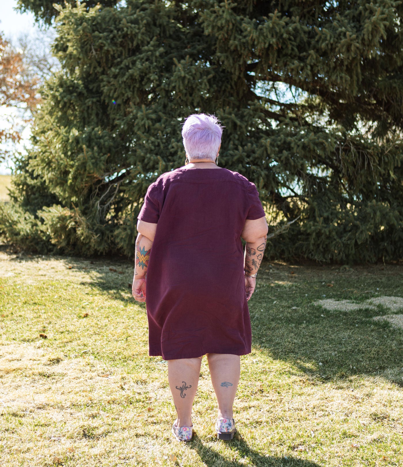 This is an image of Yolanda standing with her back to the camera while wearing her Camber Set dress in Nomad Linen Twill in Merlo while standing in a green field.  