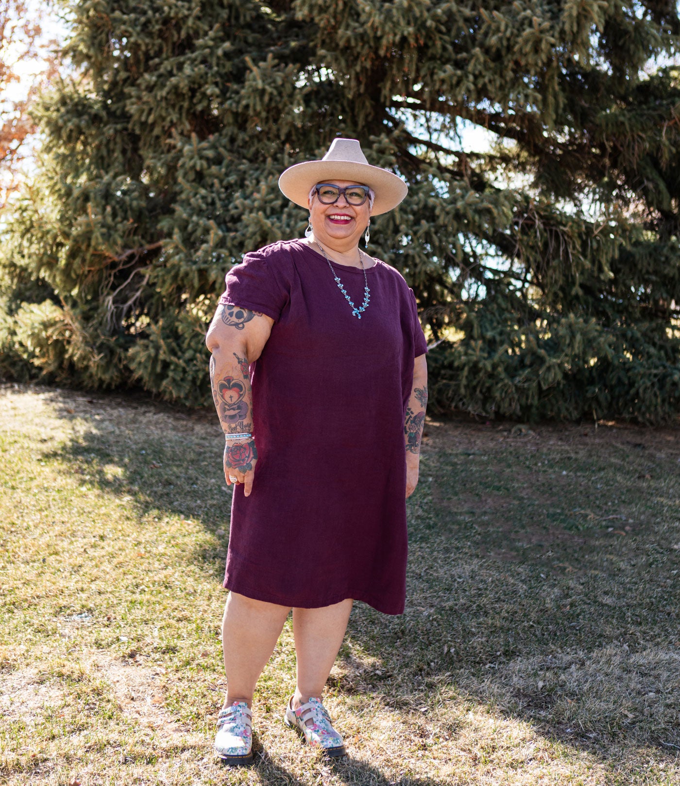 This is an image of Yolanda wearing her Camber Set dress in Nomad Linen Twill in Merlo while standing in a green field.  