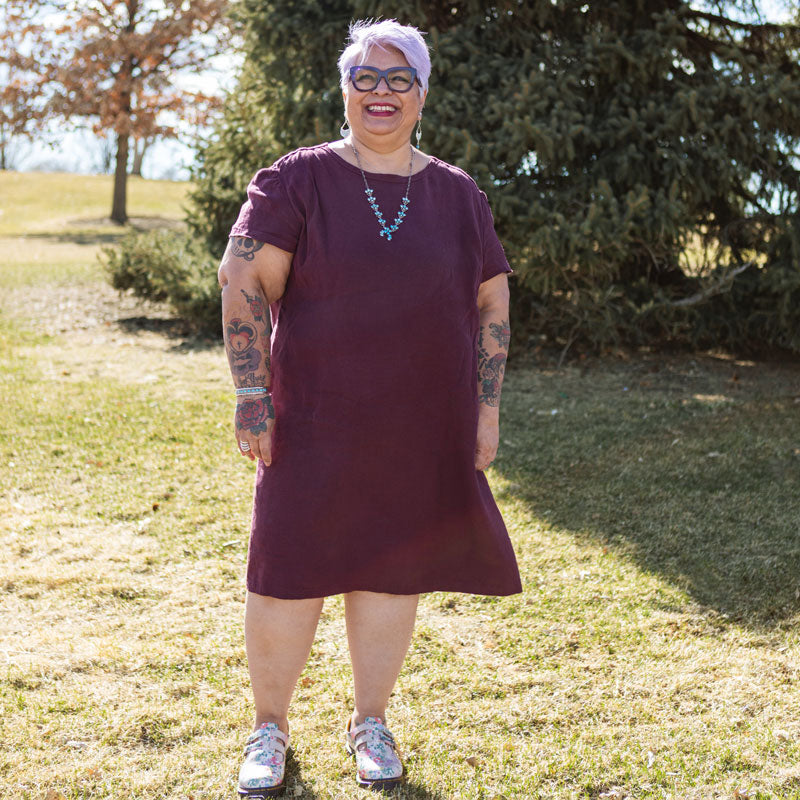 This is an image of Yolanda wearing her Camber Set dress in Nomad Linen Twill in Merlo while standing in a green field.  