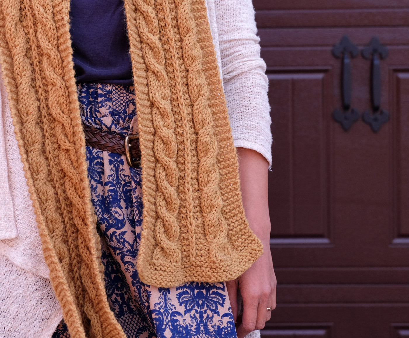 Detail of a handknit, mustard-yellow cabled scarf.