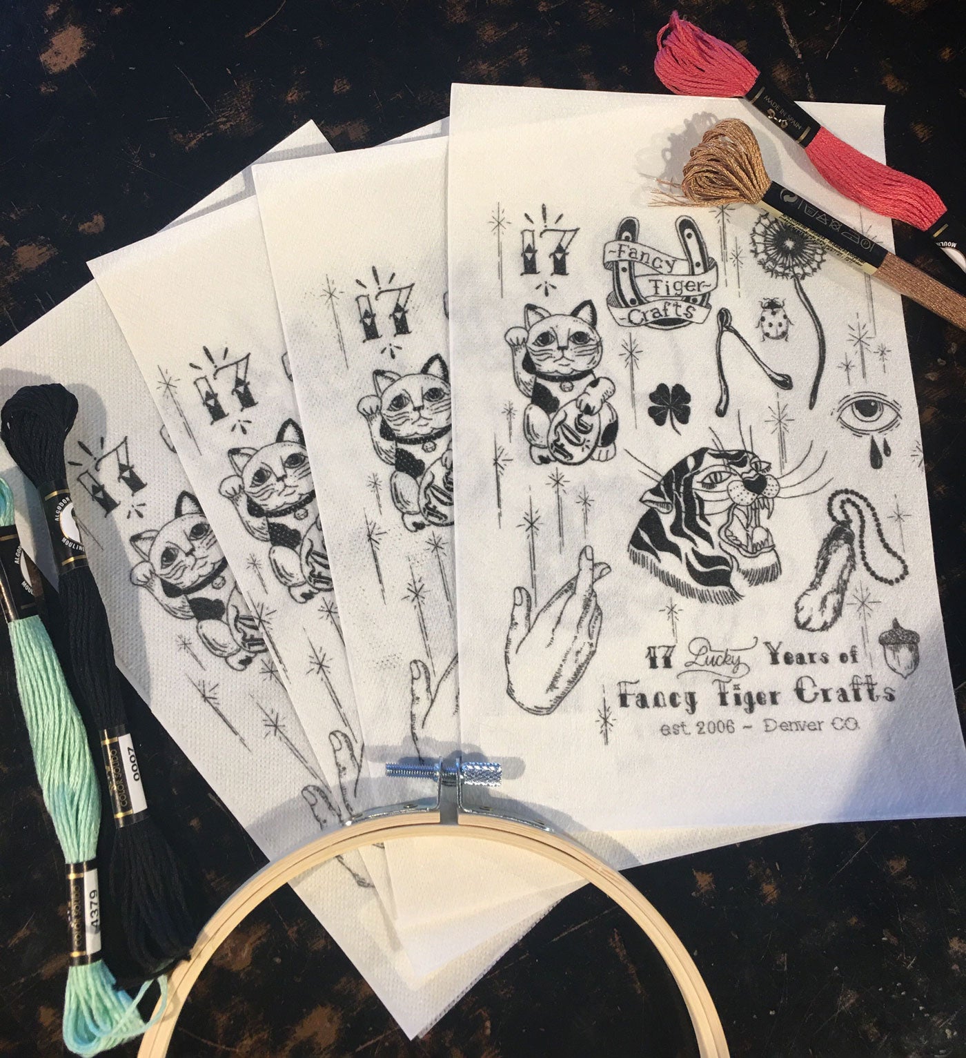 Five sheets of embroidery transfer sheets fanned out with embroidery floss and a hoop framing them