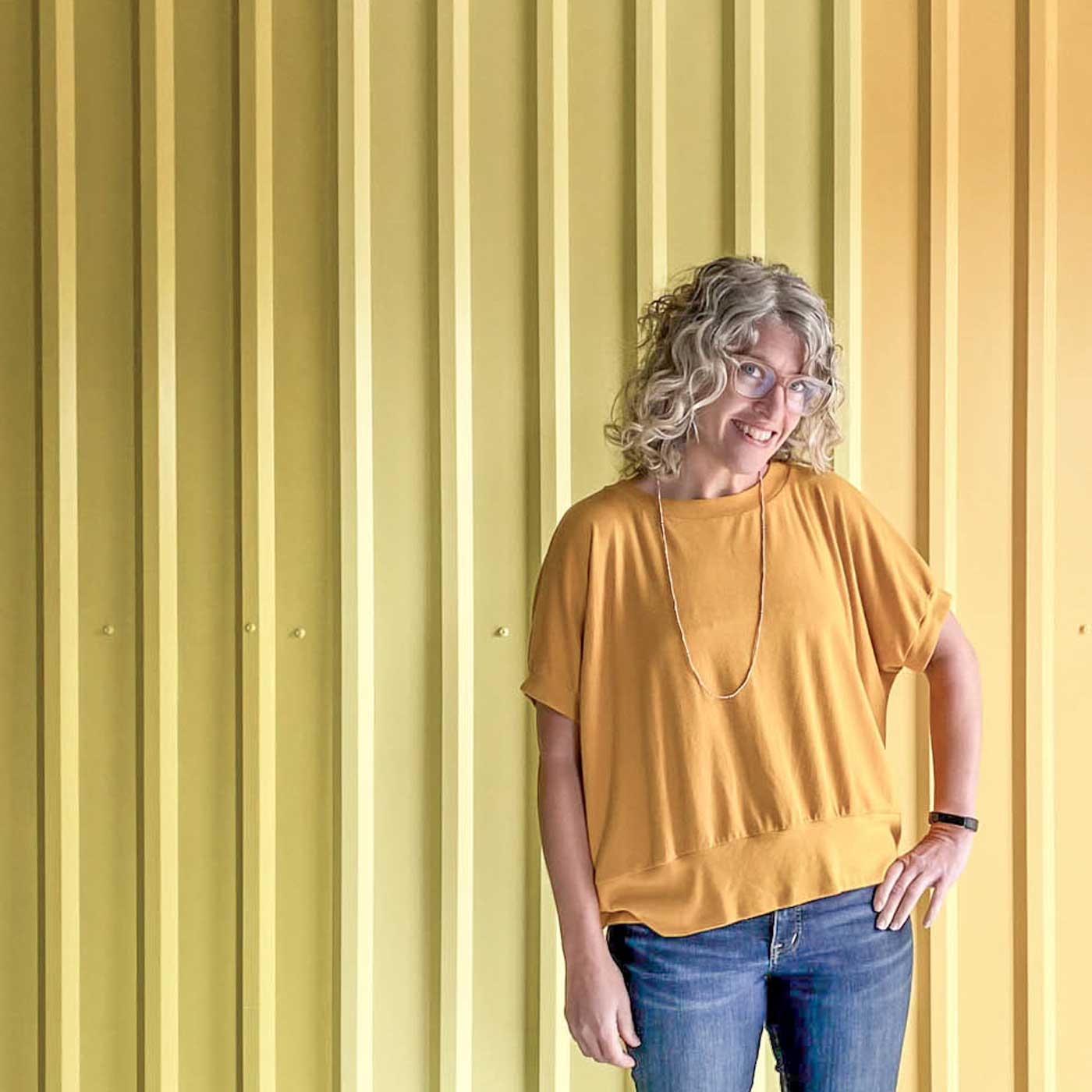 Jaime wearing a golden yellow Hosta tee standing in front of yellow ombre wall.