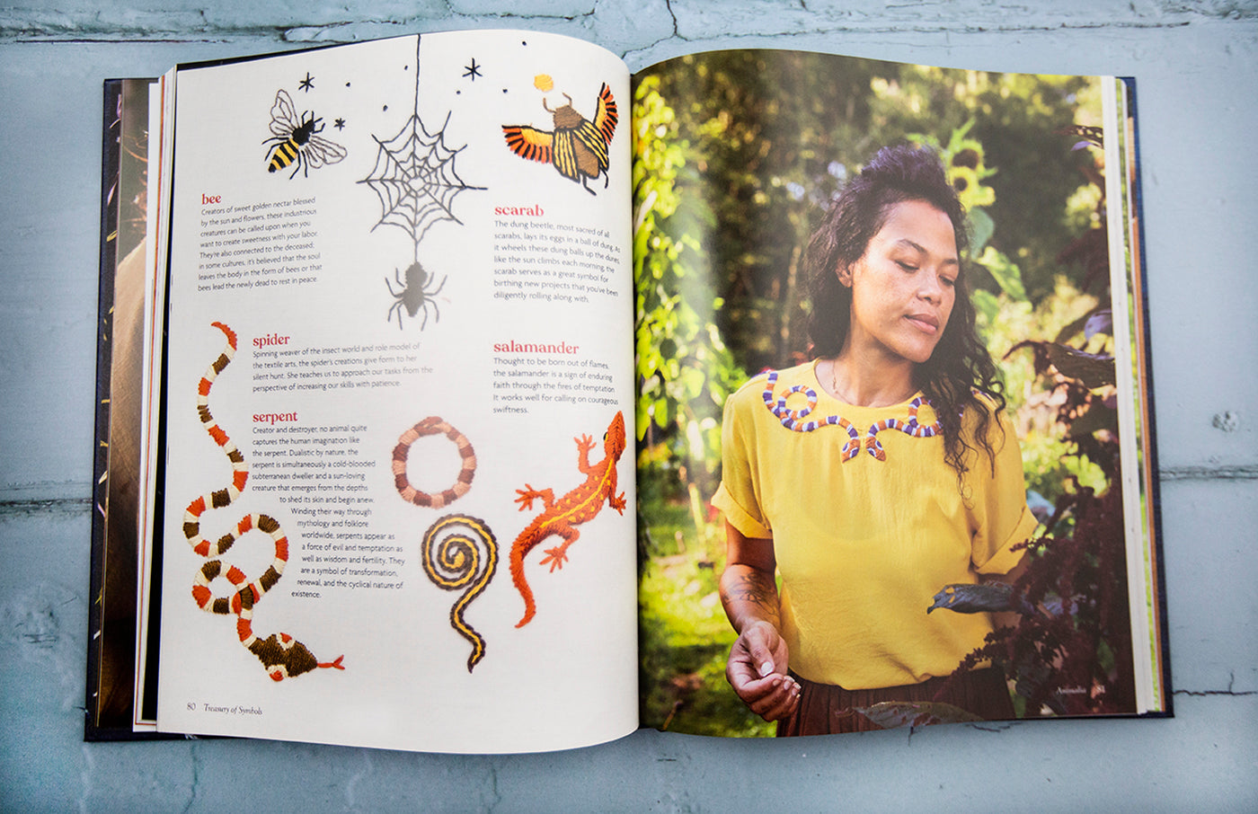 This is an image of a book opened up to two pages, one featuring a variety of embroidered symbols and one page featuring a woman wearing a yellow shirt that has some of those symbols on her shirt. 