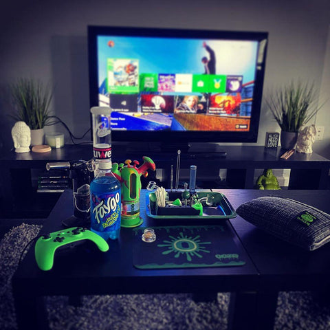 A shot of a living room from the couch. In front is a coffee table filled with different Ooze smoking products including the Rasta Trip and dab mat, and there is a tv with the Amazon FIre Stick home screen on in the background.