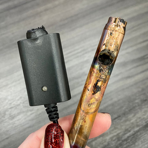 A rose gold Ooze Slim Twist Vape Battery has been burned and severely damaged from overheating due to use of a non-Ooze charger. The charger is also next to the battery, and the connector has been melted.