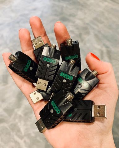 A white female hand holds a handful of black Ooze Smart USB Chargers above a gray floor.