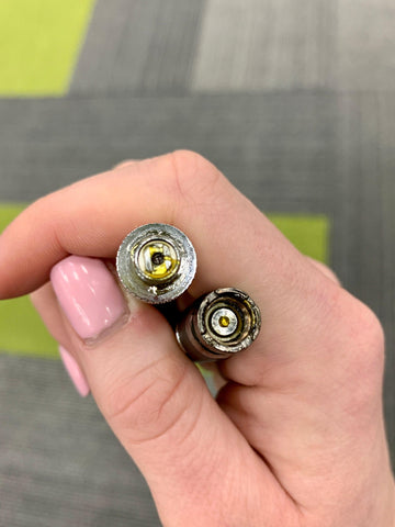 A white woman with light pink nail polish holds an oil cartridge and Ooze Vape Battery in her hand to show where both pieces connect. The cartridge is leaking oil and the battery connection is a bit dirty.