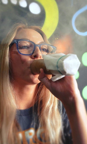 A young women with blonde hair and glasses smoking out of a sploof