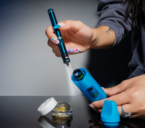 An Ooze Twist Hot Knife 2.0 is loading a dab into a blue electro barrel. The LED light on the tip is lit up