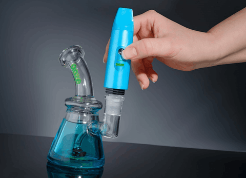 A hand is inserting a blue Ooze Booster into a blue Ooze Glyco freeze bong to use it as a torchless dab rig.