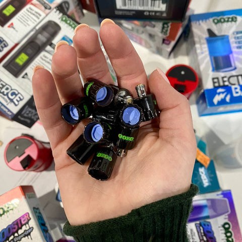 A white girl's hand is full of Ooze Onyx Atomizers with the blue Azul core dishes showing.